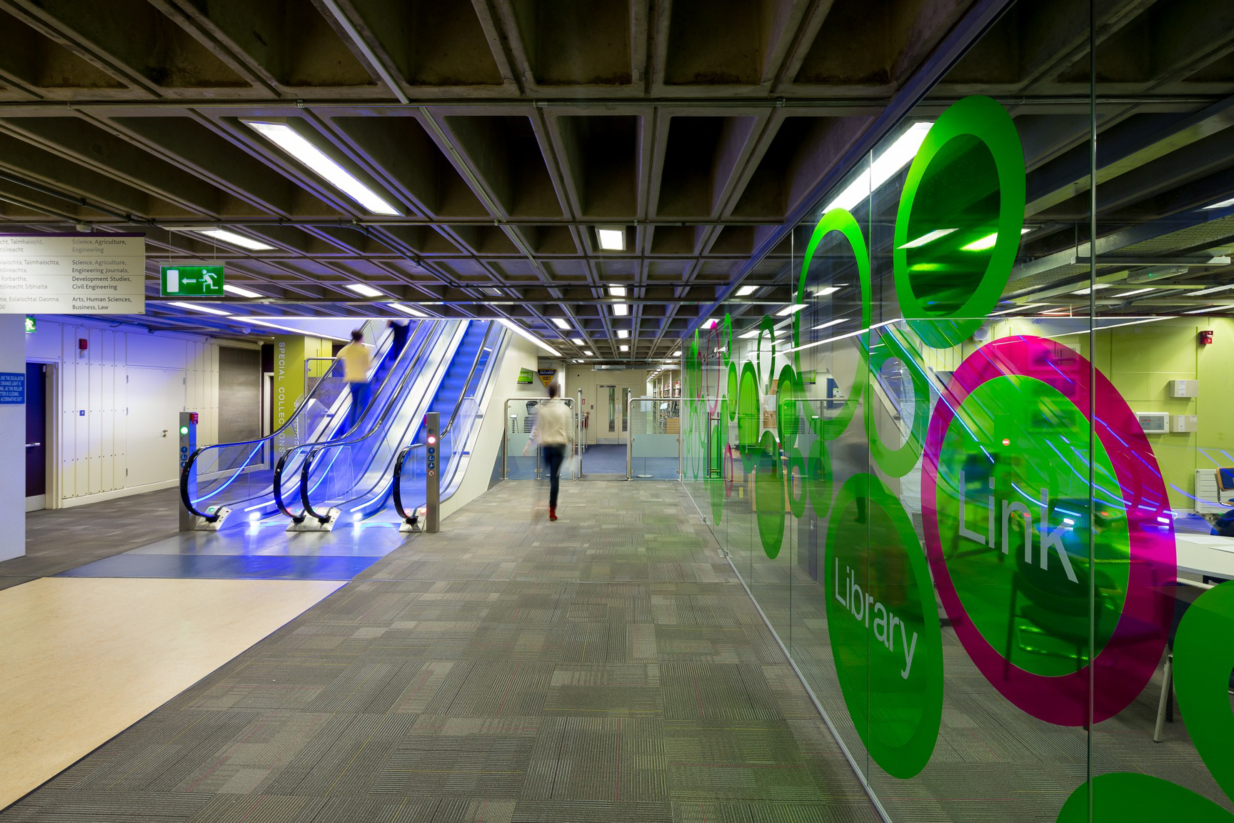 A student walking through a barrier between an escalator and a green-glass wall